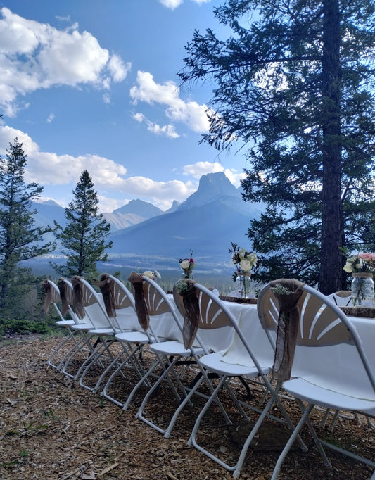 Snow white, fan back, folding chair. View with mountain backdrop.